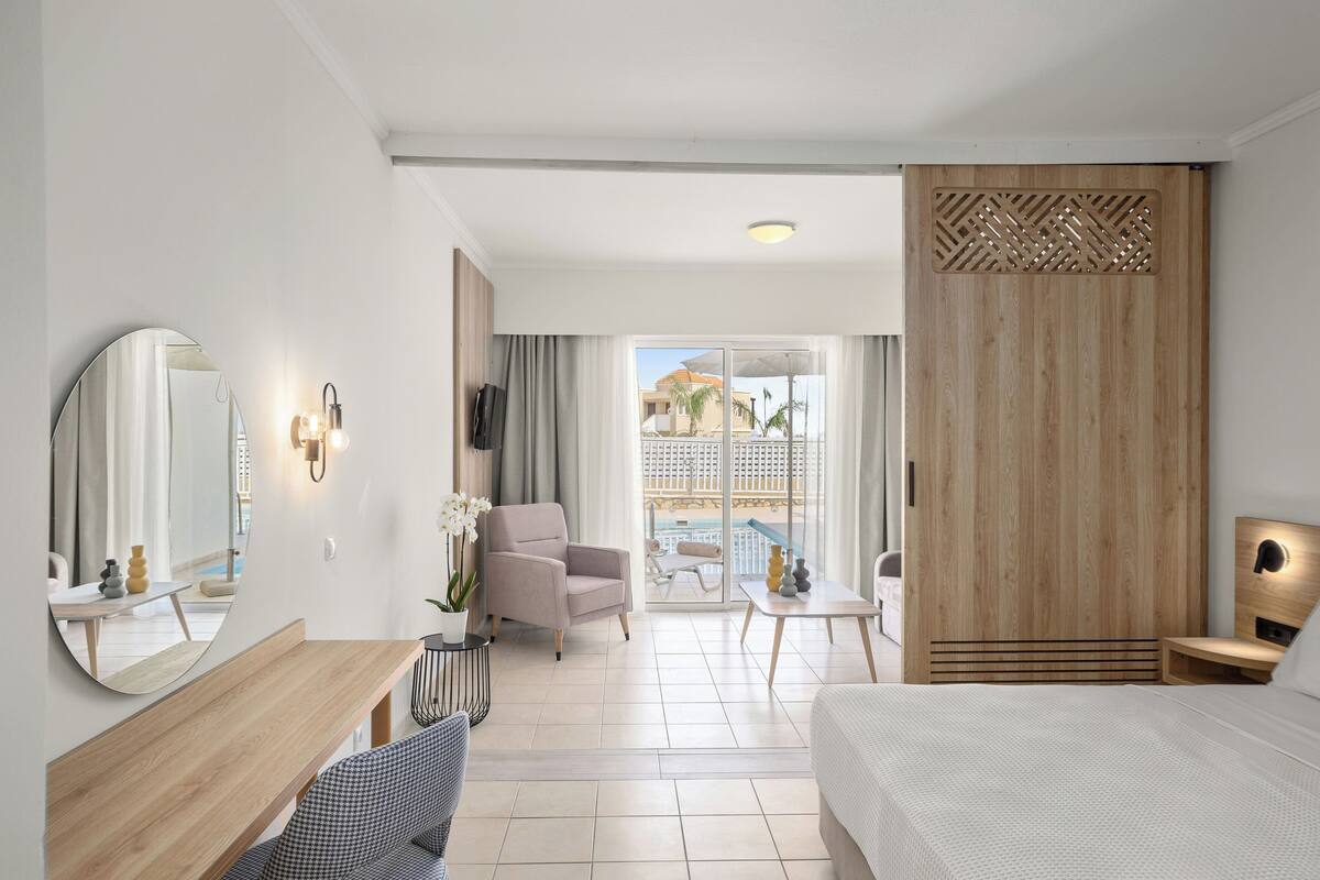 Une chambre d’hôtel moderne équipée d’un lit, d’un bureau, d’une chaise, d’un grand miroir et offrant une vue sur l’espace piscine.