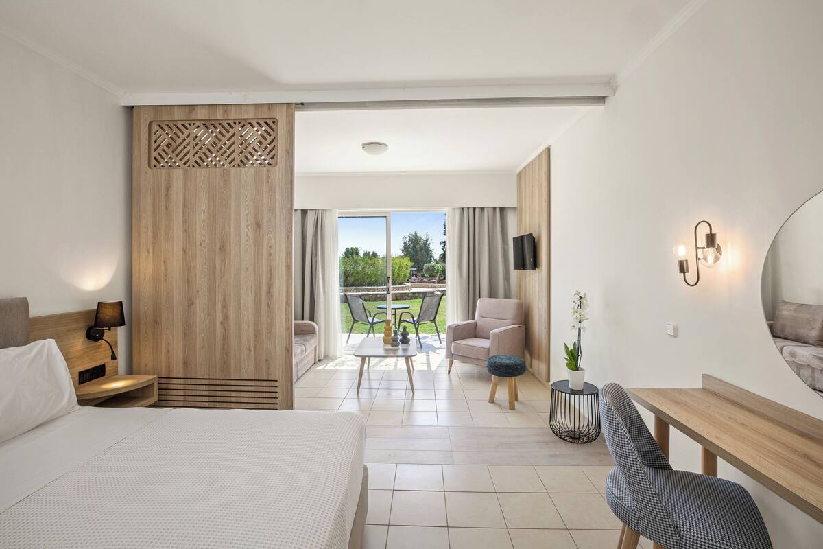 Une chambre d’hôtel moderne, dotée d’un grand lit, d’un bureau, d’une chaise et d’un balcon offrant une vue sur la verdure.