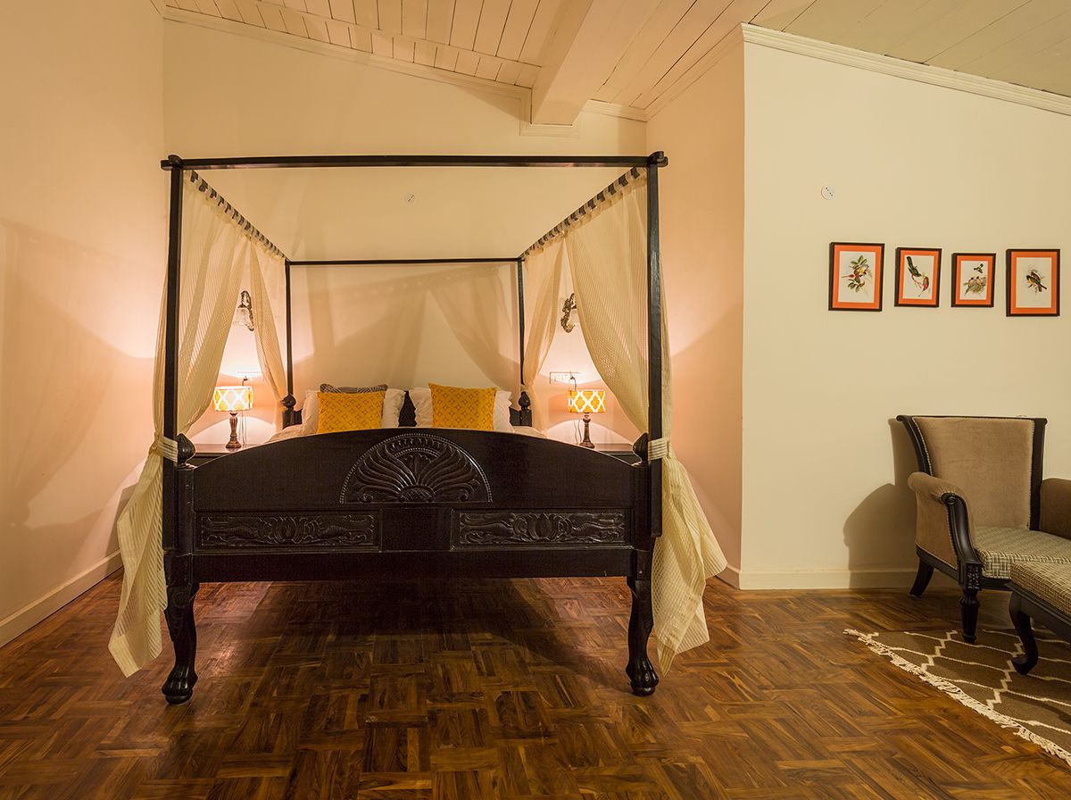 A four-poster bed with a canopy, a chair, and framed pictures on the wall.