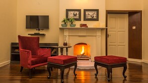 A living room with a fireplace, a television, and red upholstered furniture. - Ging Tea House (Darjeeling)