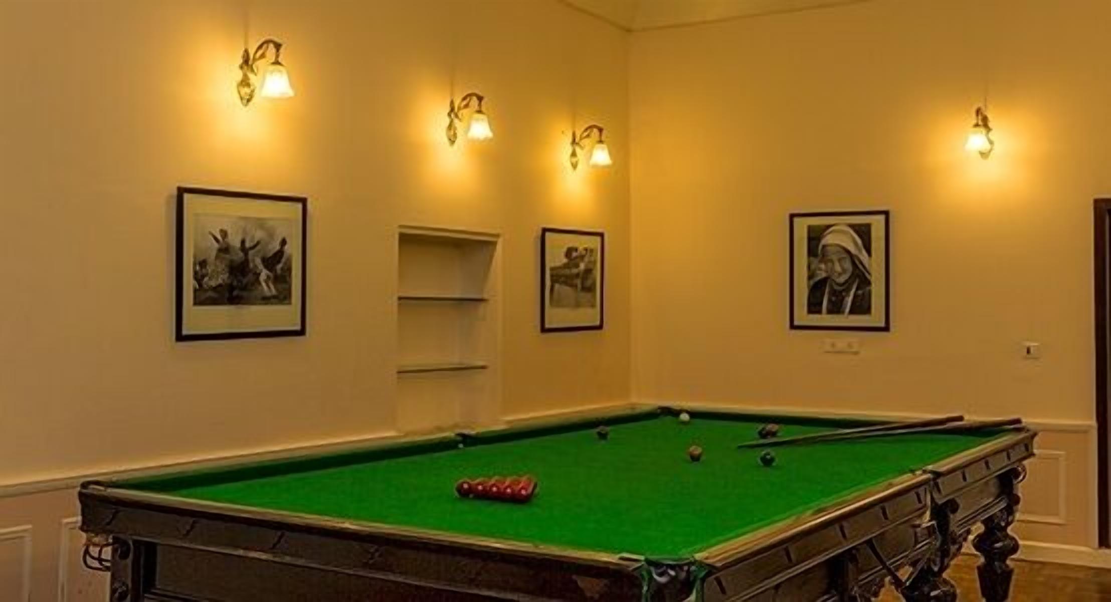 A pool table with green felt, surrounded by walls with framed pictures and wall sconces.