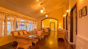 A cozy, well-lit hallway with wicker furniture, wooden floors, and large windows with curtains. - Ging Tea House (Darjeeling)