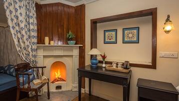 Una sala de estar acogedora con chimenea, un sofá, una mesita con lámpara y obras de arte enmarcadas en la pared.