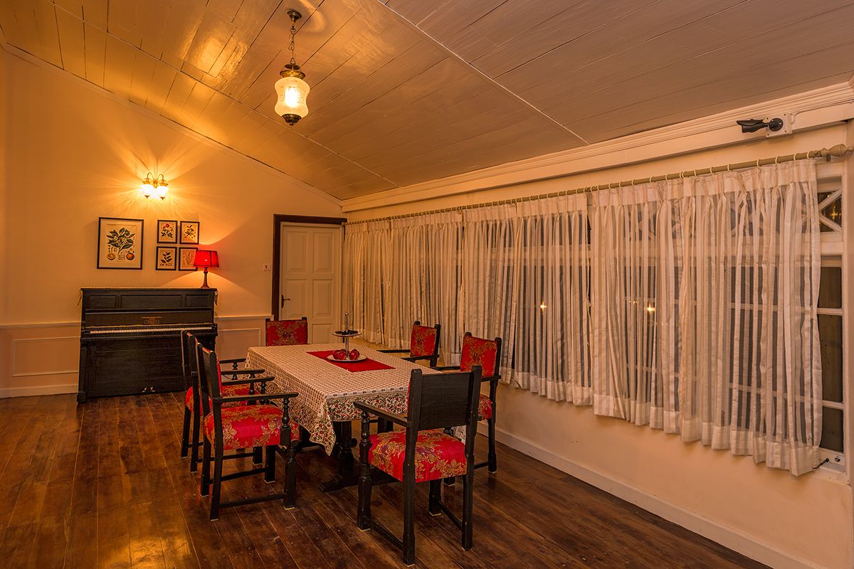 A dining room with a wooden table, red upholstered chairs, a piano, and a window with sheer curtains.