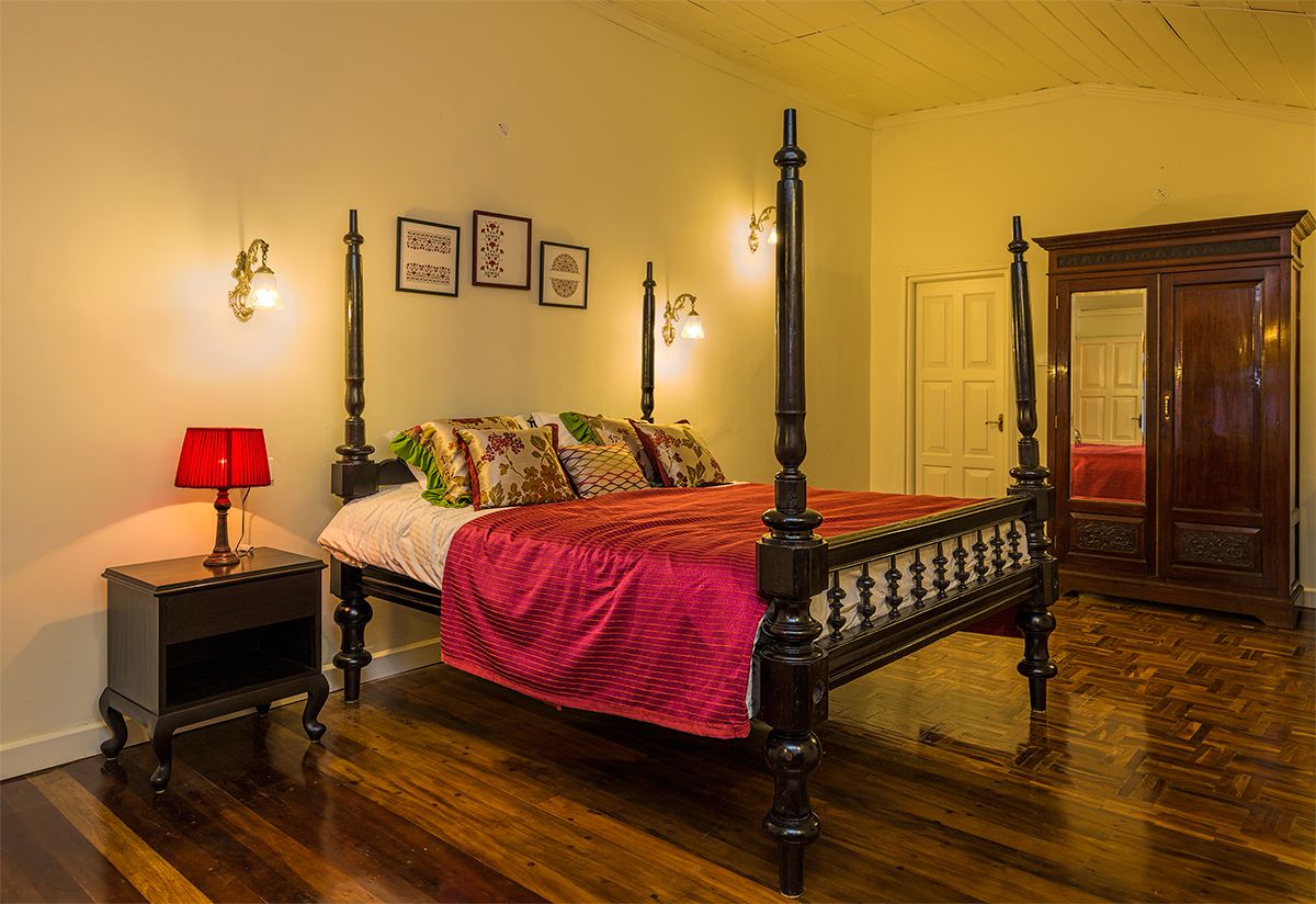 Una cama con dosel, con un cubrelecho rojo, una mesita de noche con una lámpara roja y un armario de madera.