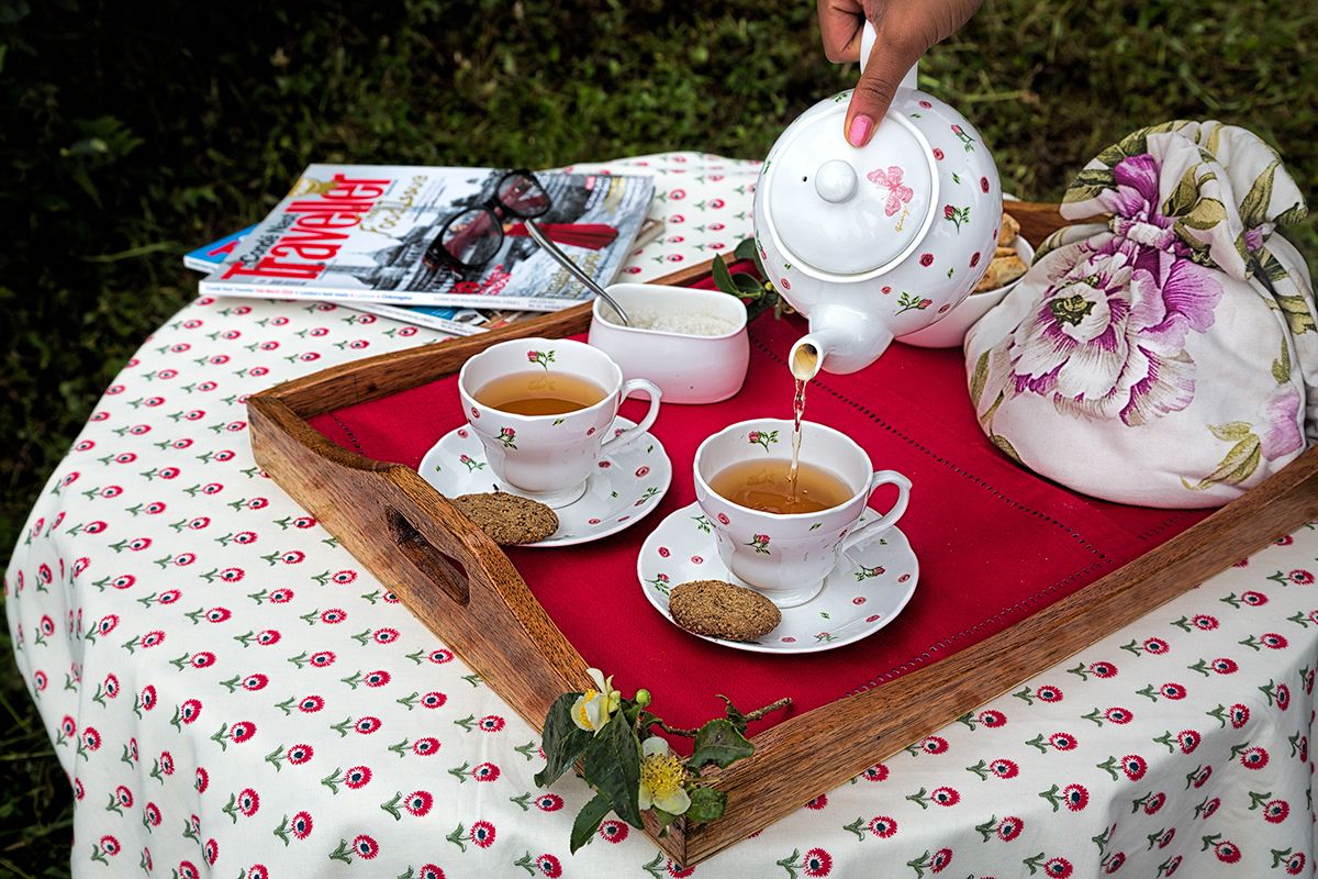 Ein Picknick mit Tablett, Teekanne, Tassen und einer Zeitschrift auf einer blumigen Tischdecke.