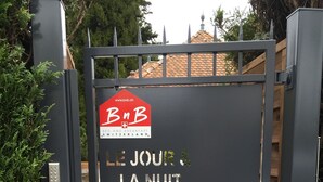 Un cancello in metallo nero con un cartello che riporta “Le Jour & La Nuit” e un indirizzo web.