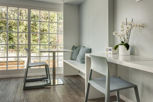 A modern room with a large window, a white desk, two chairs, a bench with cushions, and a potted orchid. - Le jour et la nuit (Geneva)