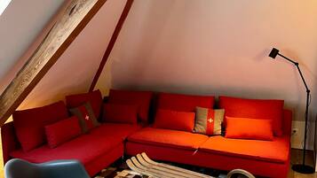 Ein gemütliches Loft-Zimmer mit einem roten Ecksofa, einem blauen Schaukelstuhl und einem karierten Teppich.