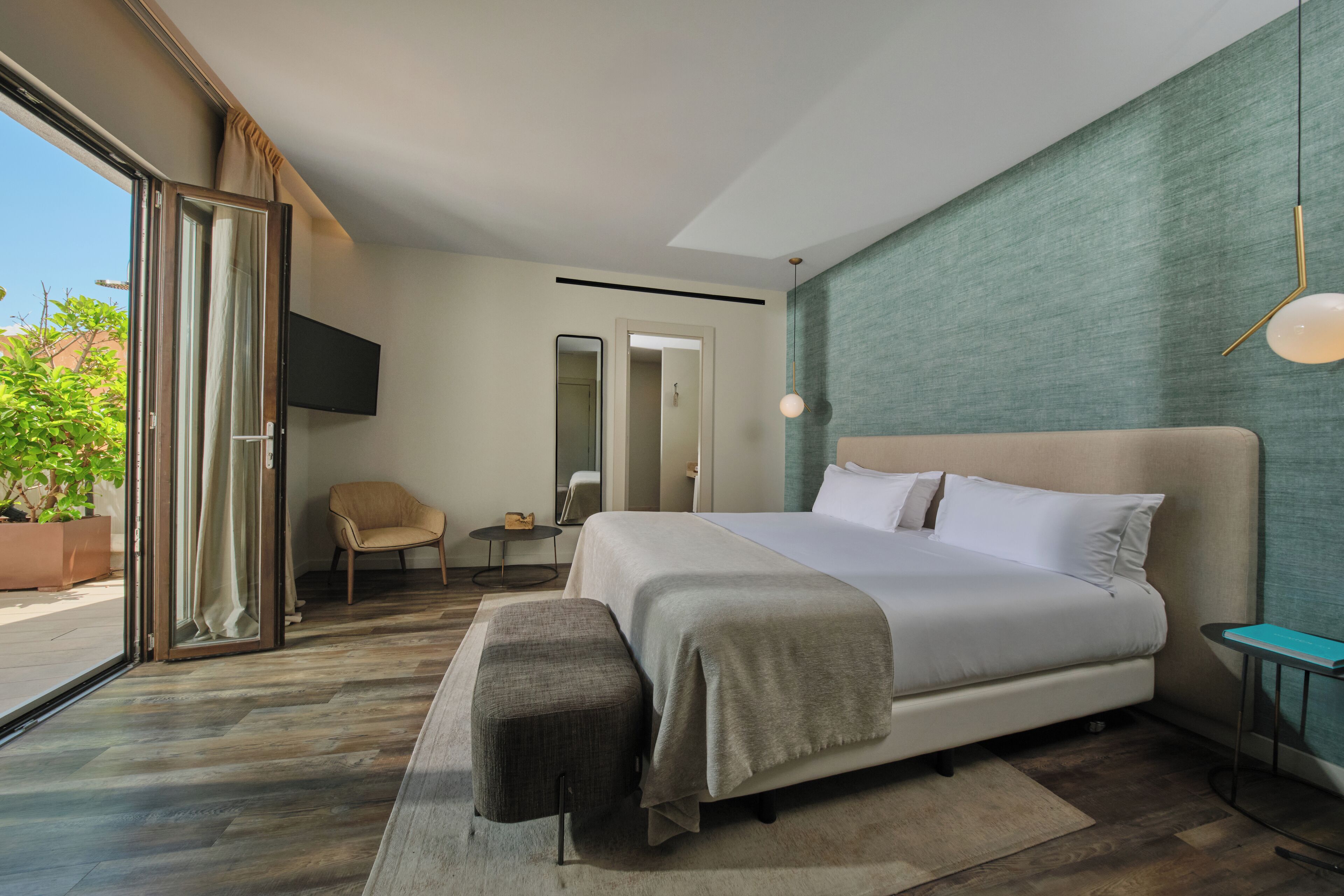Habitación de hotel moderna con una cama grande, zona de estar, televisor y vistas al exterior.