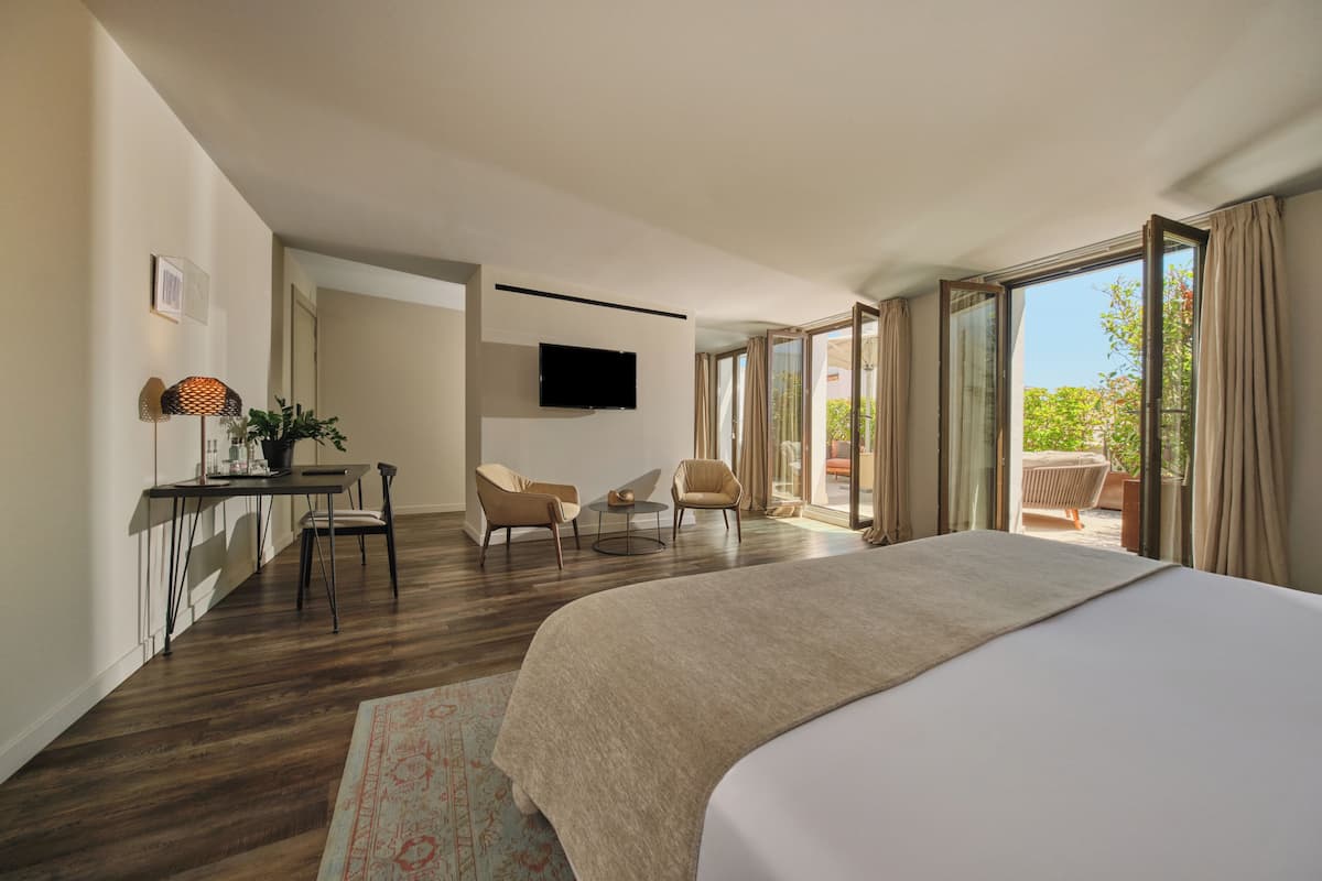 Habitación de hotel moderna con una cama grande, un escritorio con silla, televisión y balcón con vistas.