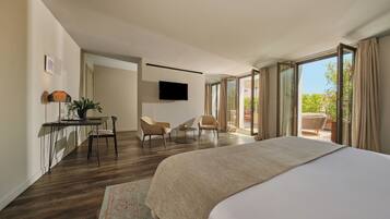 Quarto de hotel moderno com uma cama grande, uma escrivaninha com cadeira, televisão e varanda com vista.