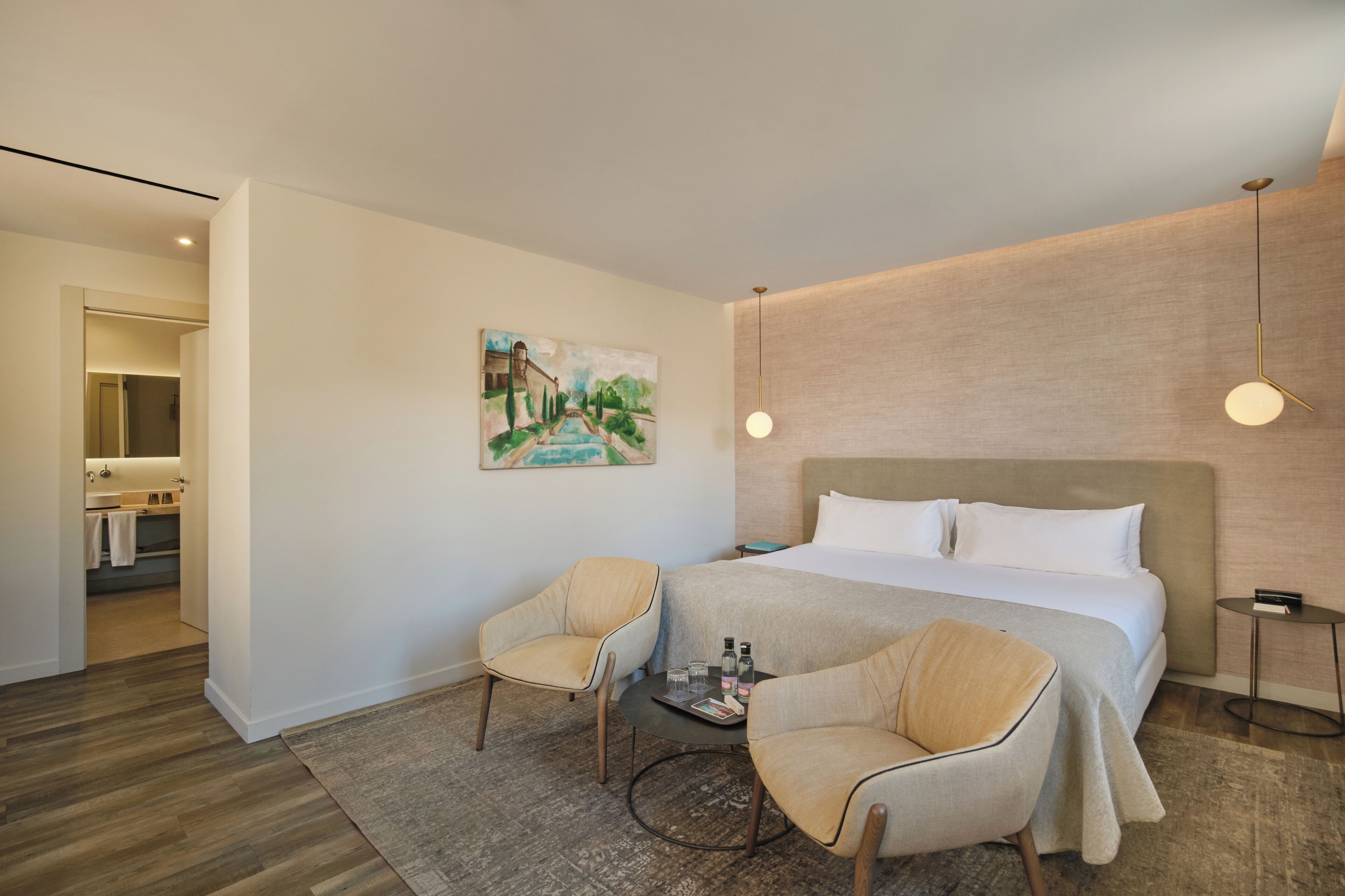Een hotelkamer met een groot bed, twee fauteuils, een kleine tafel met verzorgingsproducten en een schilderij aan de muur.