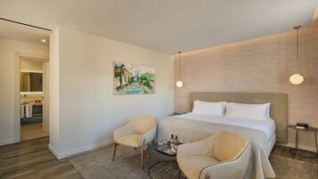 Een hotelkamer met een groot bed, twee fauteuils, een kleine tafel met verzorgingsproducten en een schilderij aan de muur.