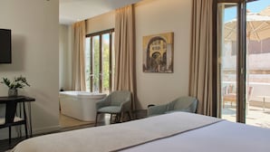 Una habitación de hotel con una cama grande, una bañera, una silla y un cuadro en la pared.