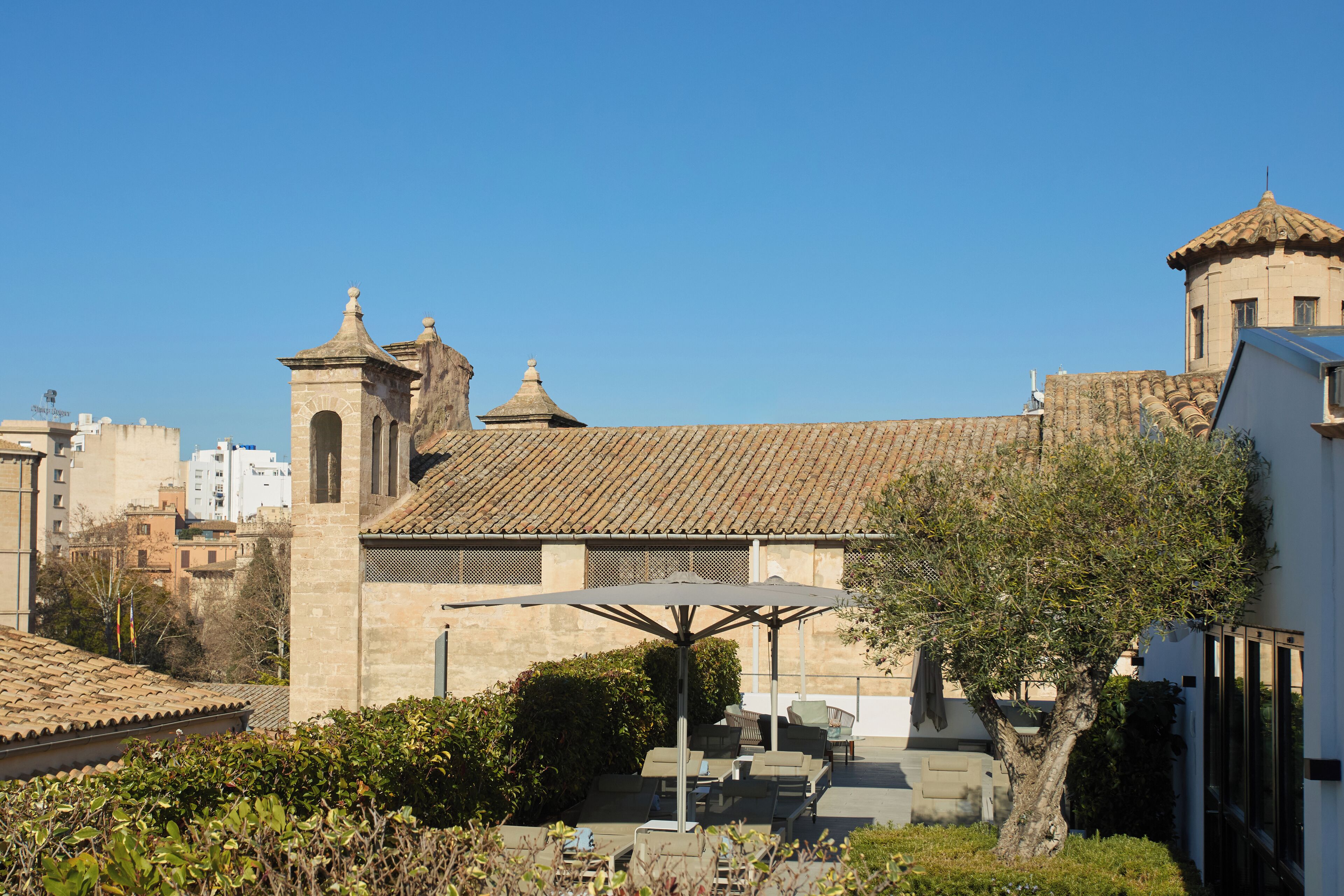 A building with a tiled roof, a bell tower, and a covered outdoor seating area with umbrellas.