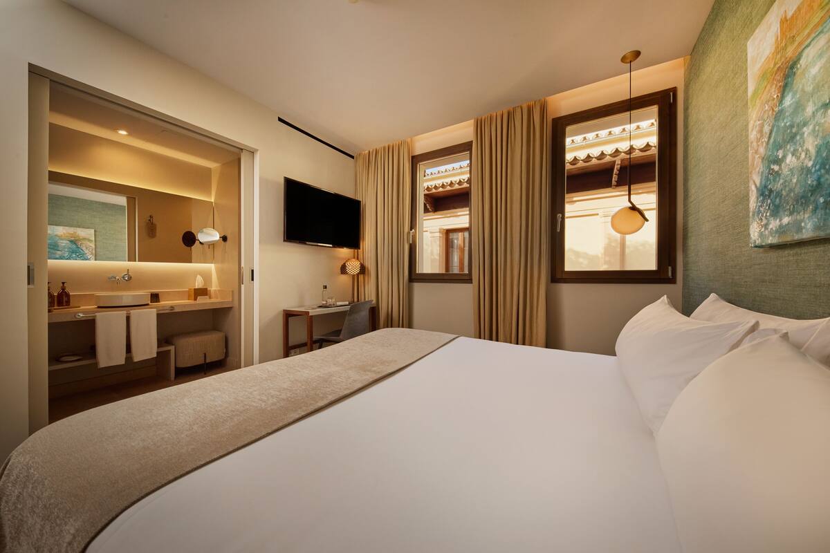 Una habitación de hotel moderna con una cama grande, un escritorio, un televisor de pantalla plana y un baño con tocador y perchero para toallas.