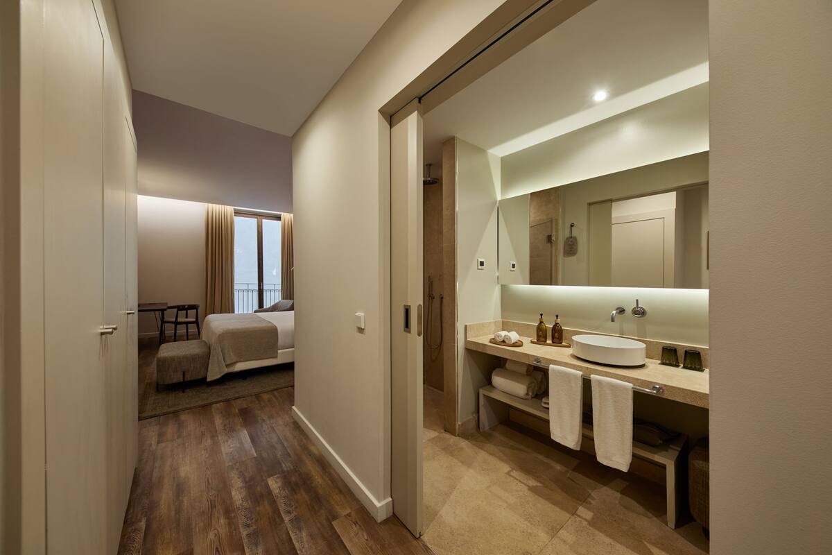 Un baño de hotel moderno con un espejo grande, un lavabo redondo y una zona de ducha.