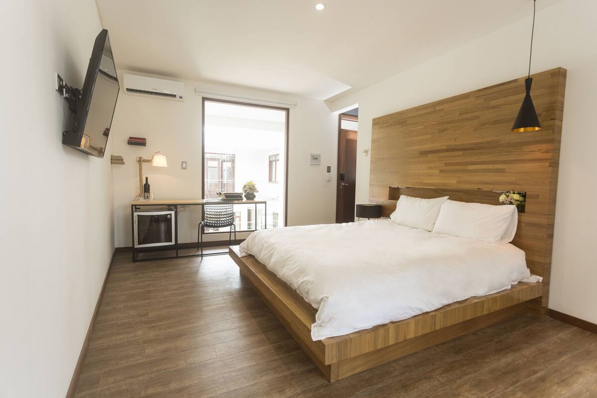A modern bedroom with a wooden bed frame, a desk with a chair, and a TV mounted on the wall.