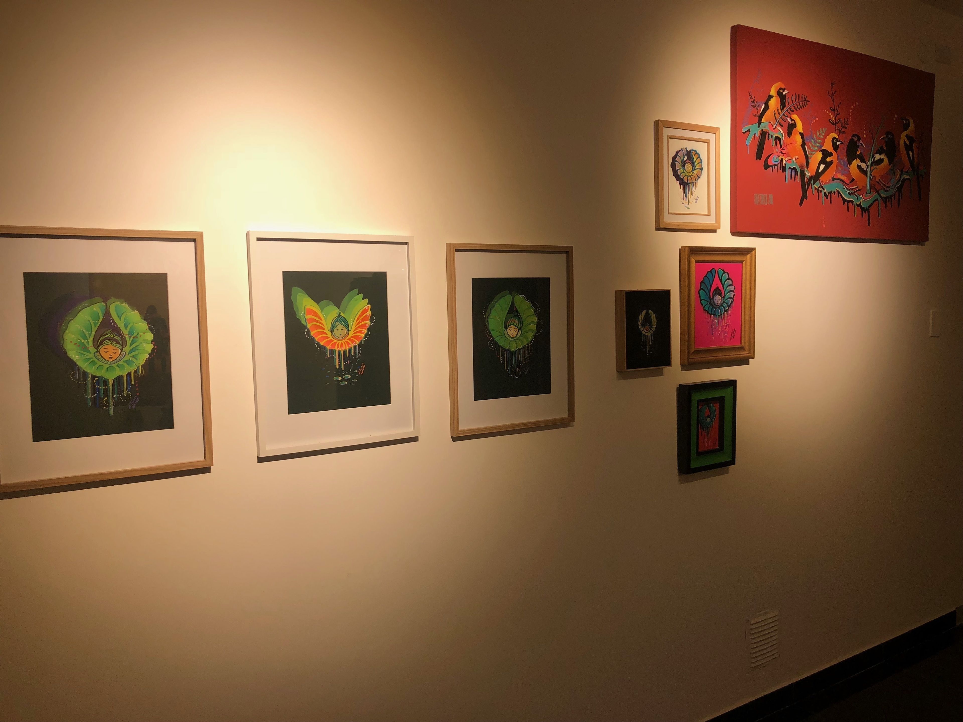 Una pared galería con obras enmarcadas, incluyendo una pieza destacada con un diseño de pájaro colorido.