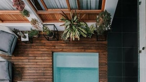 A rooftop pool area with a glass balustrade, wooden deck, and a seating area with cushions and a small table. - Cosmopolitano Hotel Boutique (Santa Cruz)