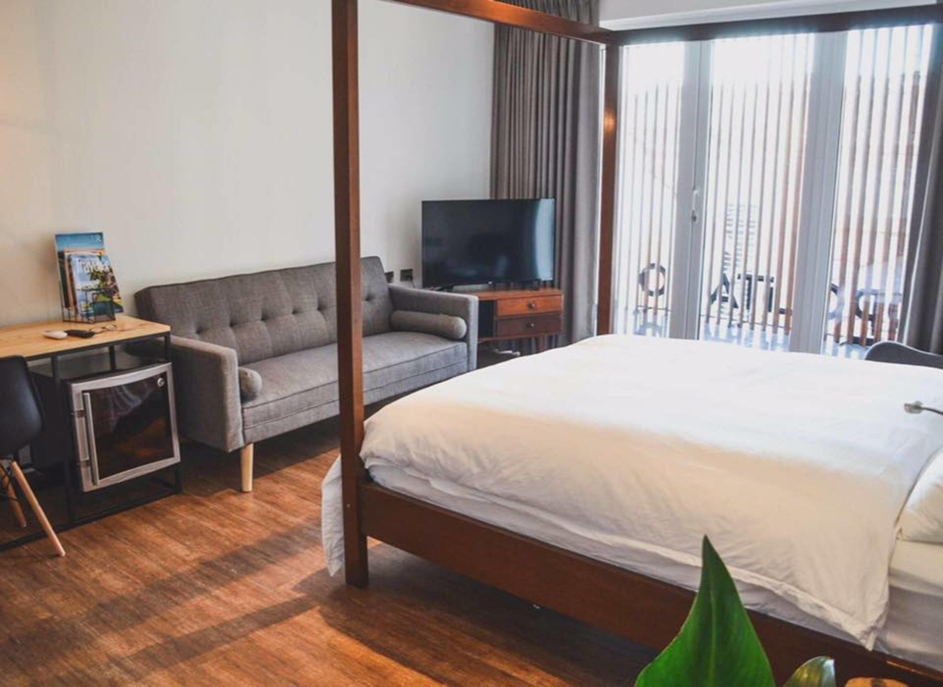 Habitación de hotel con una cama grande, un sofá, un escritorio con computadora, un televisor y un balcón con vistas.