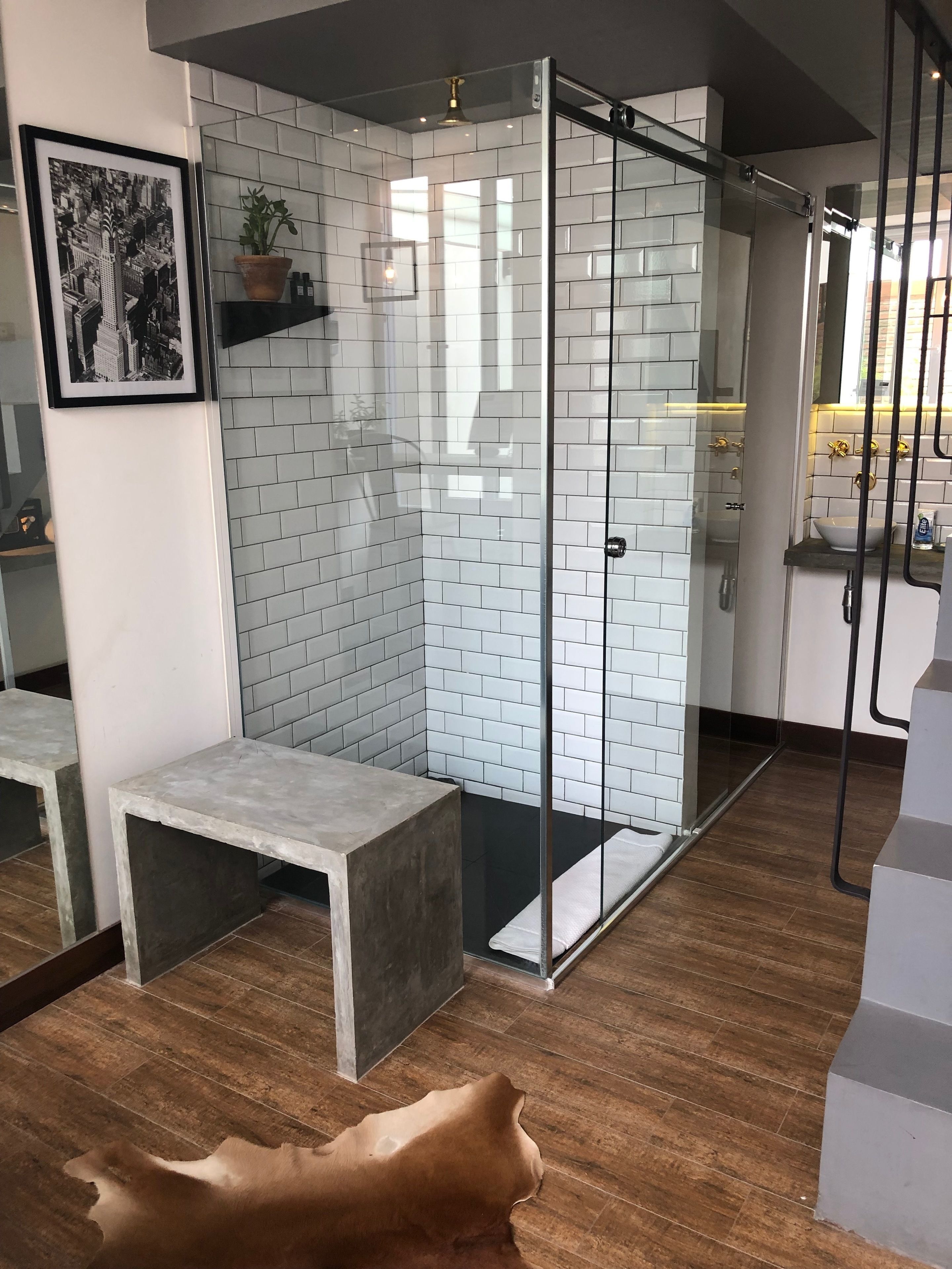 A modern bathroom with a glass shower enclosure, white tiled walls, and a wooden floor.