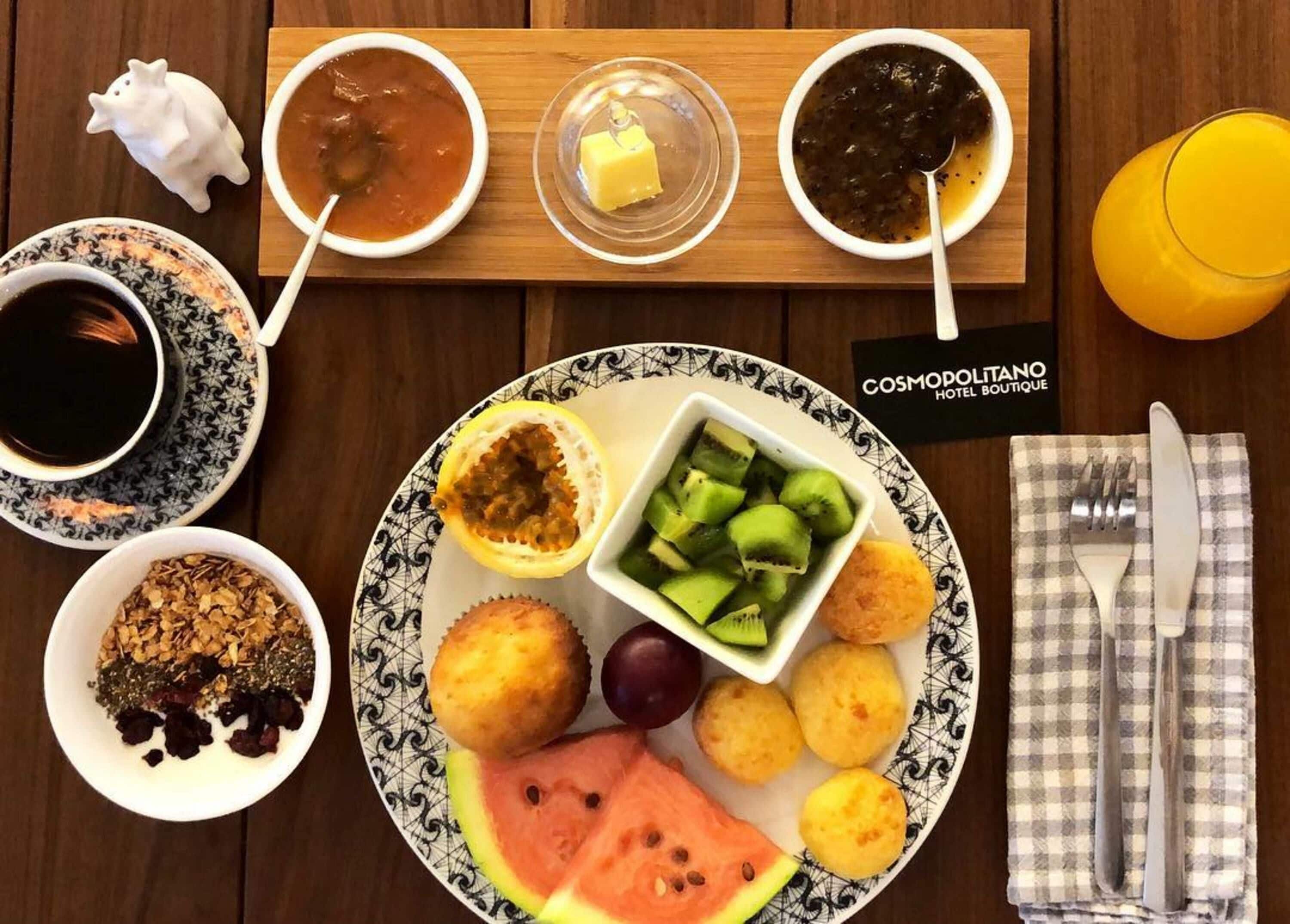 Et bord med et udvalg af retter, herunder en tallerken med vandmelon, kiwi og brød, en skål suppe og en kop kaffe.