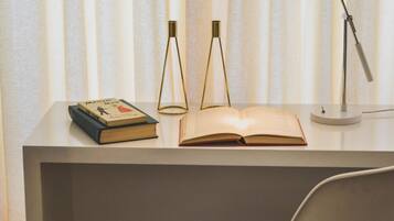 A desk with a chair, an open book, two lamps, and a pair of books on the desk.