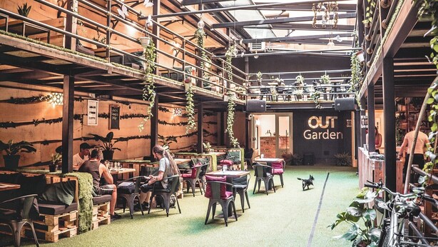 An indoor-outdoor dining area with wooden tables and chairs, hanging plants, and a sign reading "OUT Garden". - Chillout Hostel Zagreb (Zagreb)