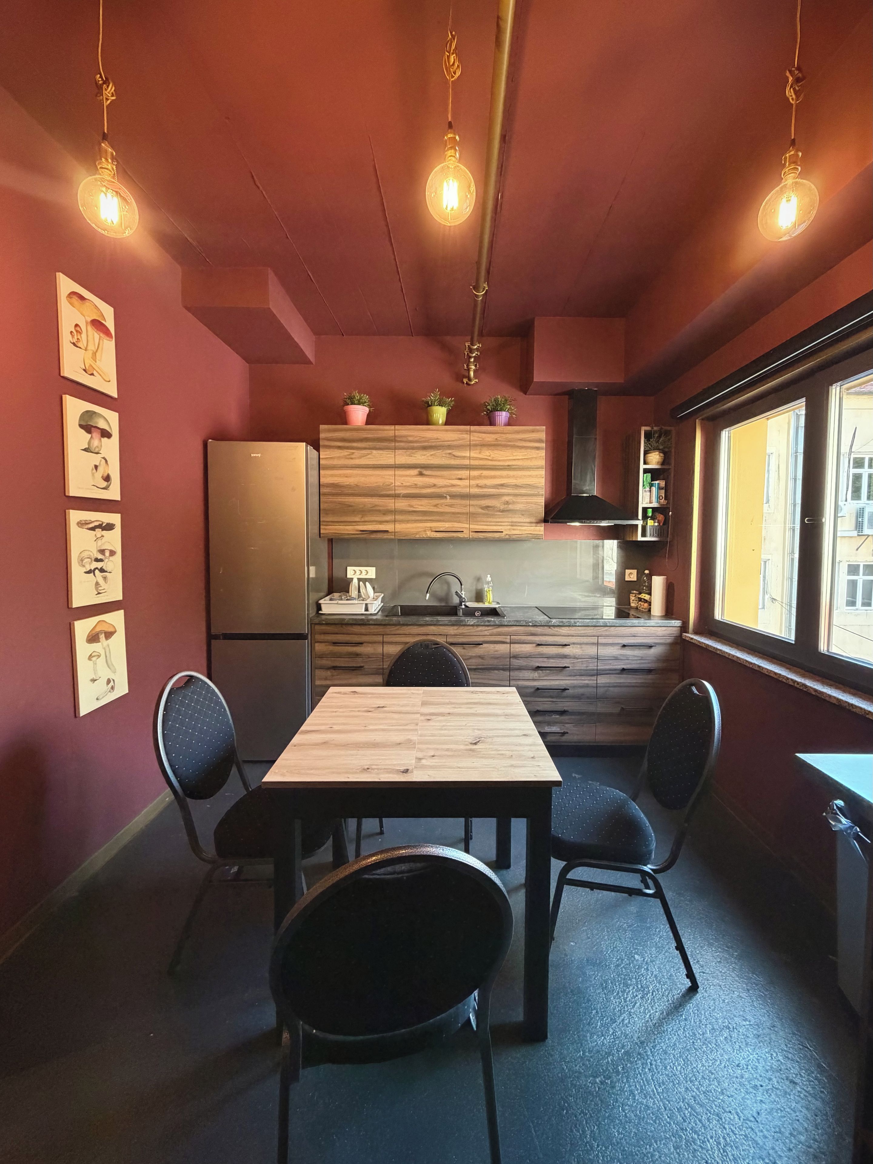 A compact kitchen with a wooden table and chairs, a refrigerator, and a window with a view.