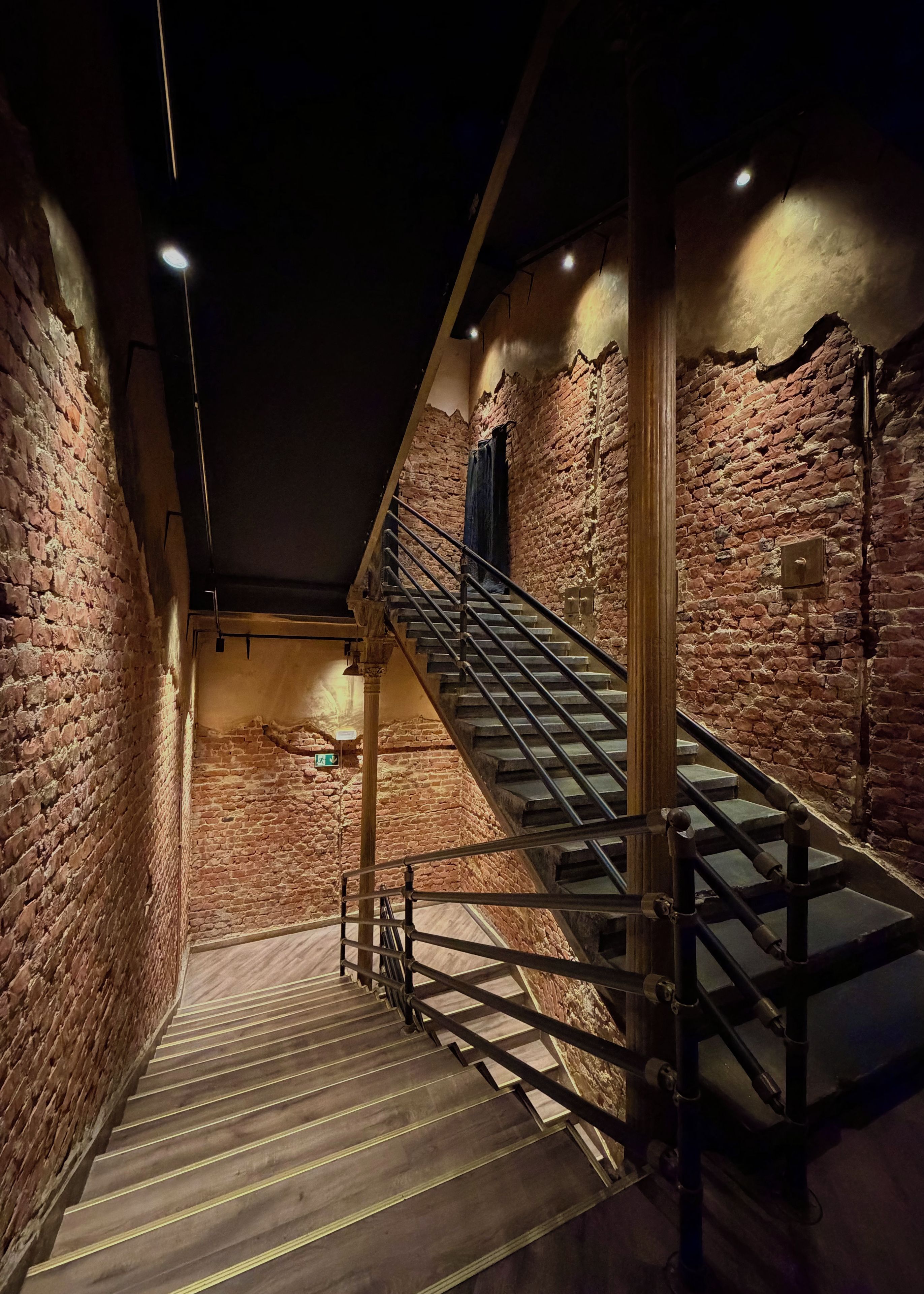 A staircase with metal railings leading up to a landing, surrounded by brick walls.