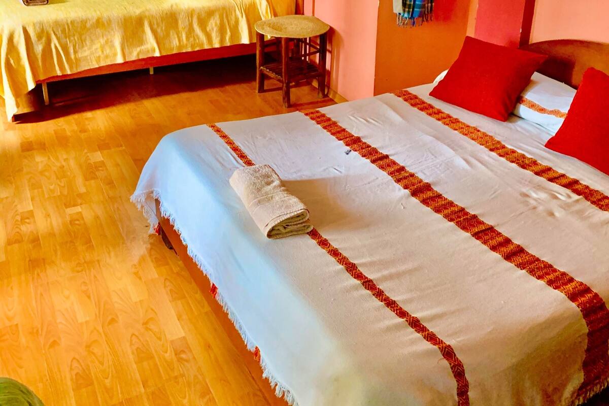 A hotel room with two beds, a wooden floor, a small table, and a window with curtains.