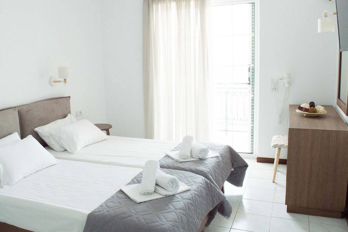 A hotel room with two beds, a small desk, and a bathroom visible through the window.