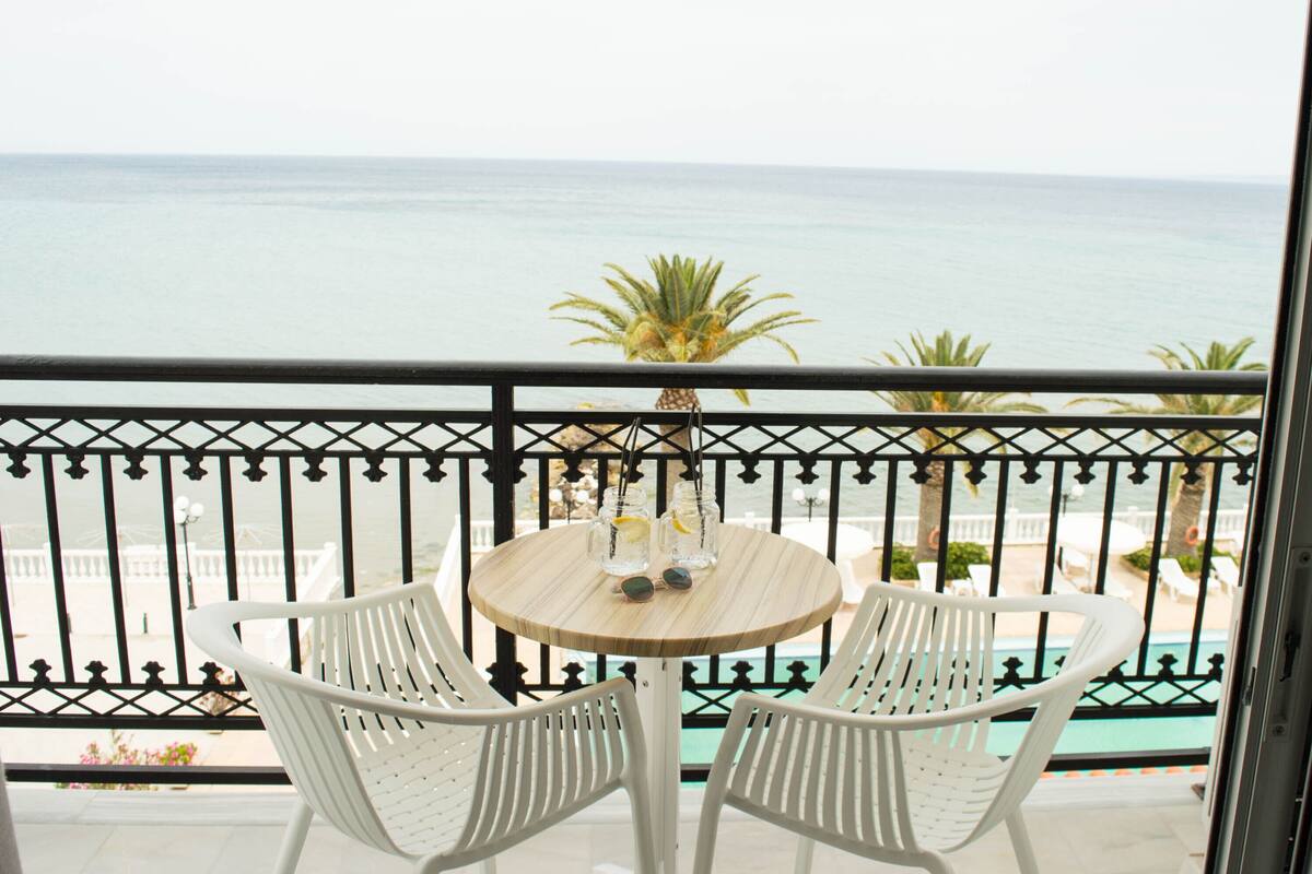 A balcony with a view of the ocean, featuring a round table with two chairs and a small potted plant.
