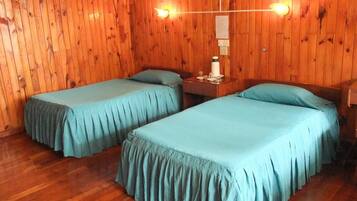A room with two beds, wooden walls, a nightstand with a lamp, and a mirror.