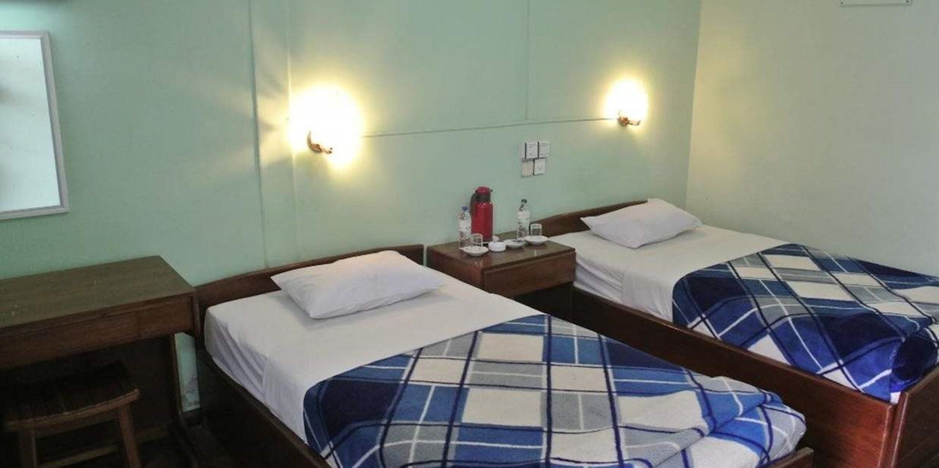 A twin room with two single beds, a wooden desk, and a small table with a water bottle and glasses.