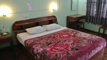 A bedroom with a bed, two bedside tables, a nightstand, a wooden headboard, a floral bedspread, and a window with curtains.