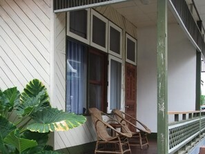 A porch with two wicker chairs, a wooden door, and large green plants. - Nanda Wunn Hotel - Hostel (Nyaungshwe)