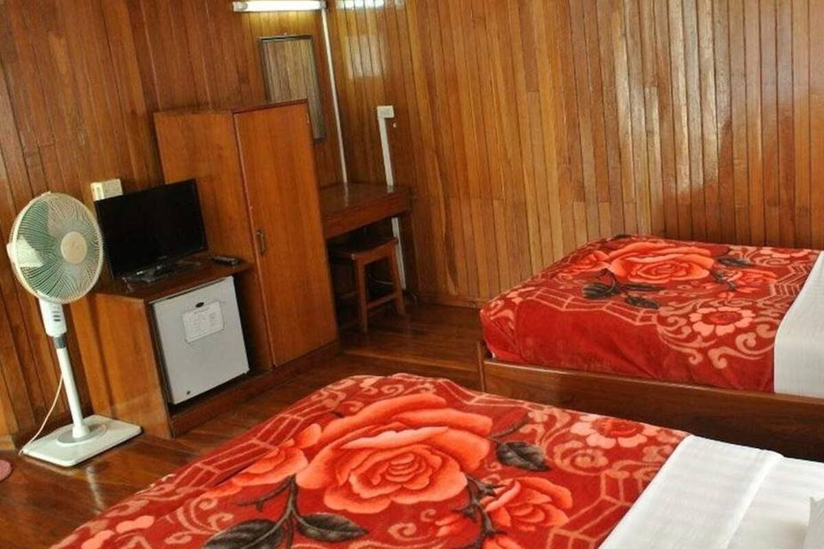 Ein Zimmer mit zwei Betten, einem Schreibtisch, einem Stuhl, einem Ventilator und einem kleinen Schrank.