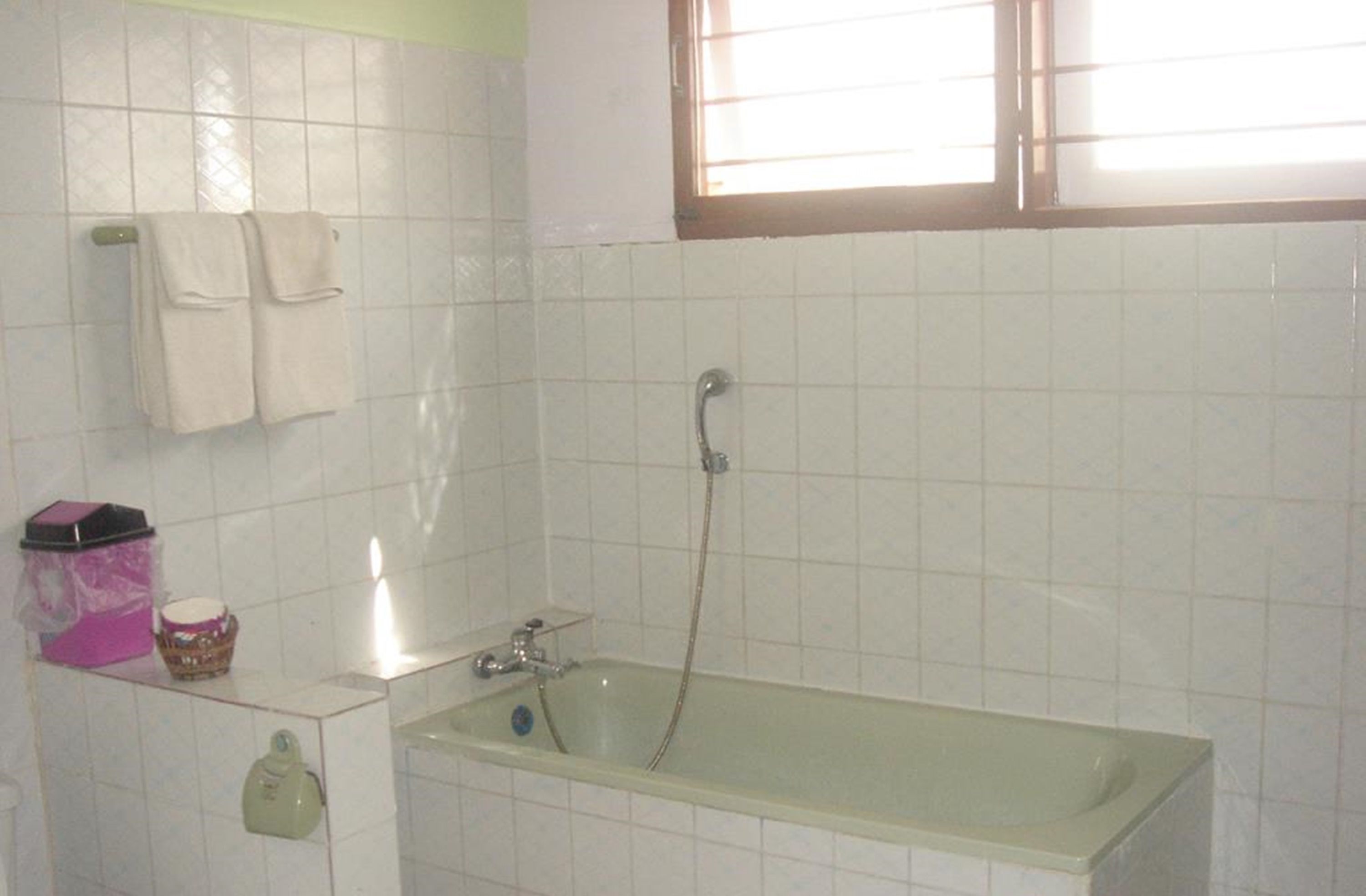 Un baño con bañera, toallero, ventana y repisas con artículos de aseo.