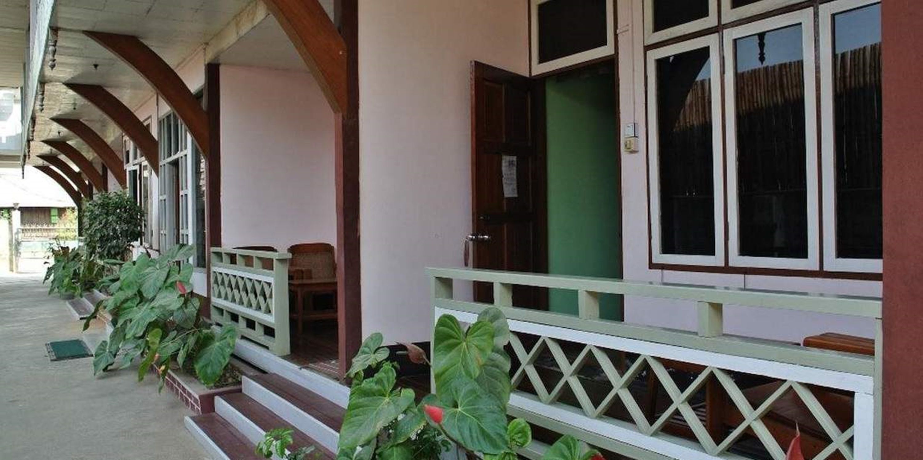 A covered porch with a wooden railing, a bench, and potted plants.