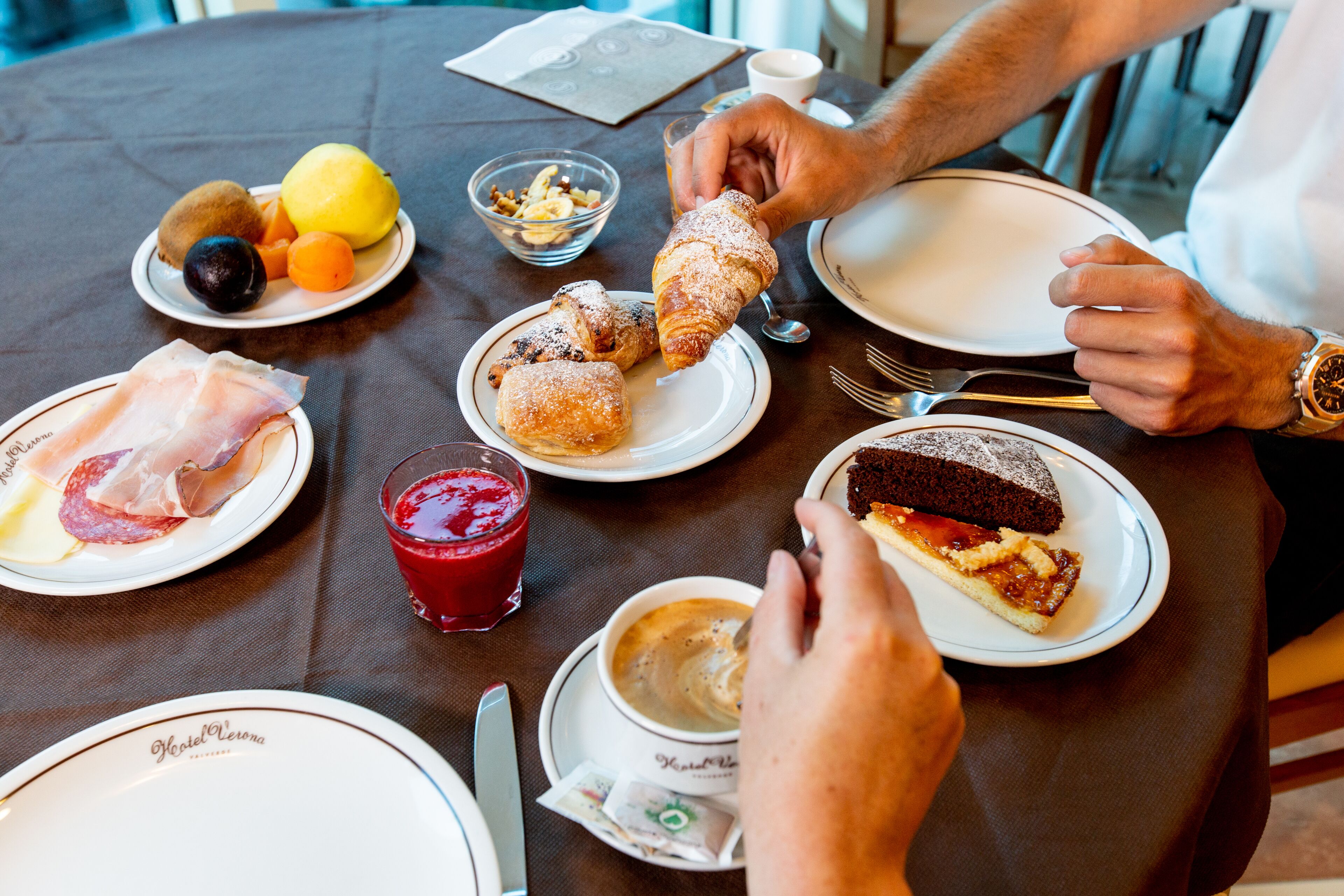 Une table à manger avec des assiettes remplies de nourriture, notamment des pâtisseries, des fruits et une part de gâteau.