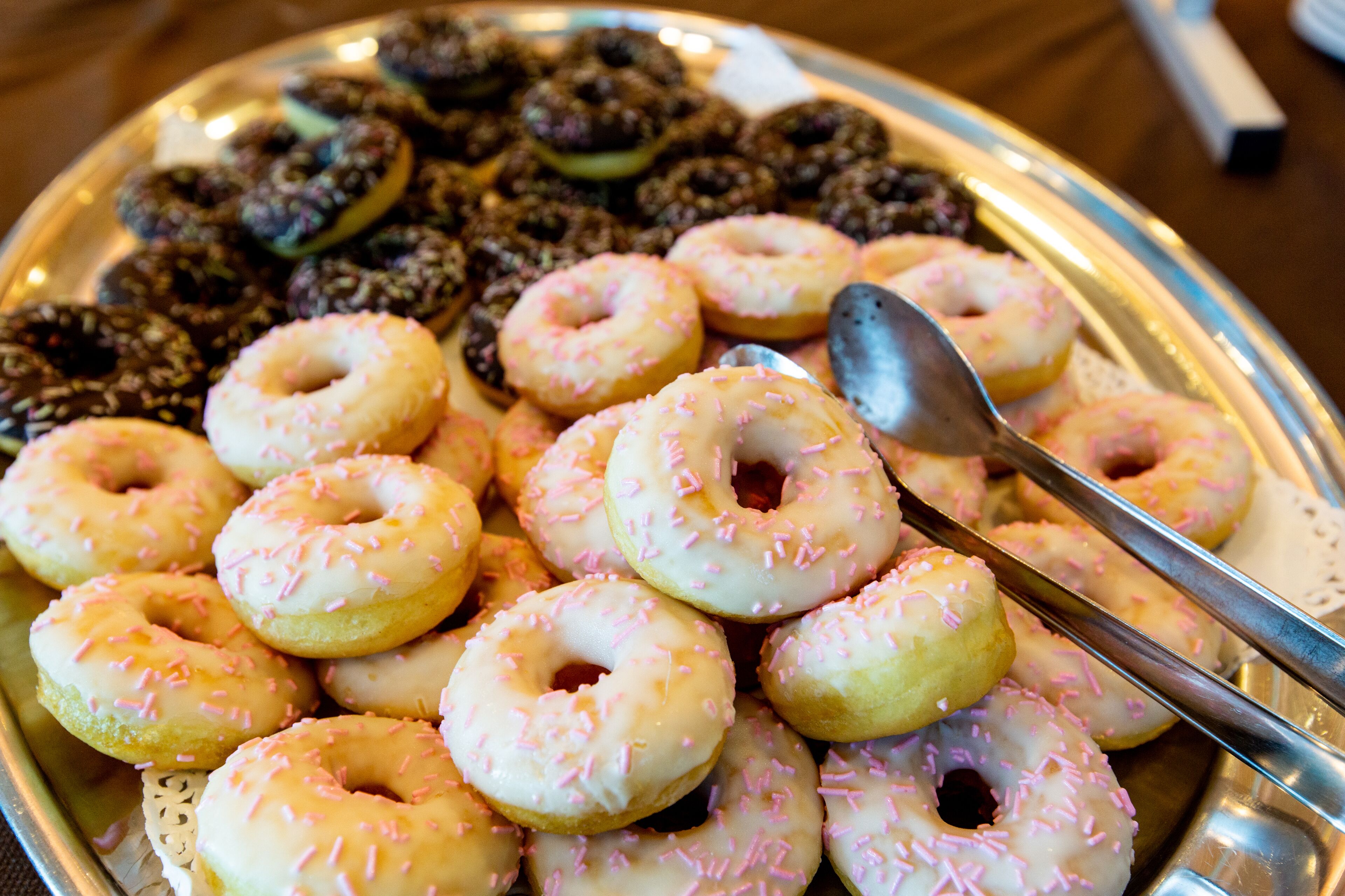 Una bandeja de donas variadas, incluyendo glaseadas y con cobertura, con una cuchara al lado.