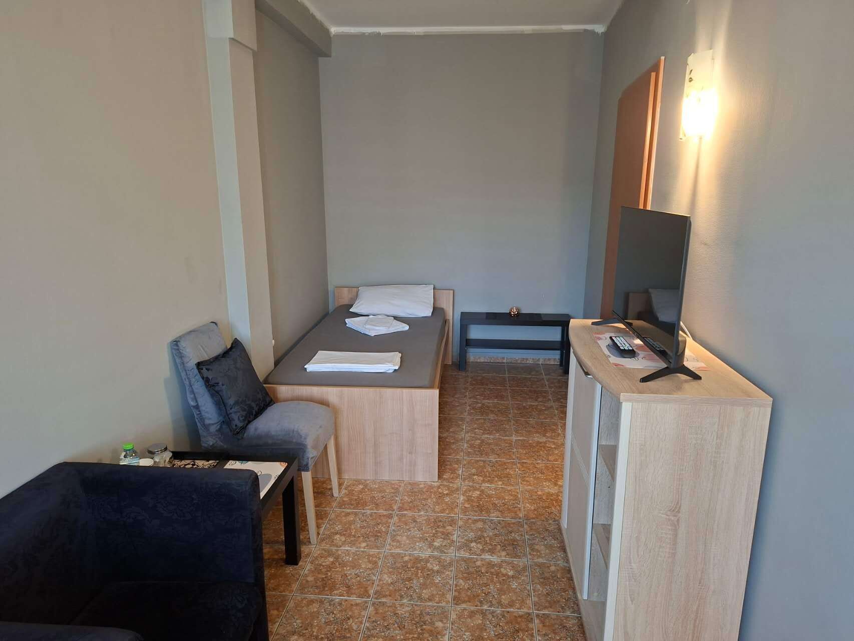 A compact hotel room with a bed, a small desk with a computer, a chair, and a sofa.