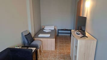 A compact hotel room with a bed, a small desk with a computer, a chair, and a sofa.