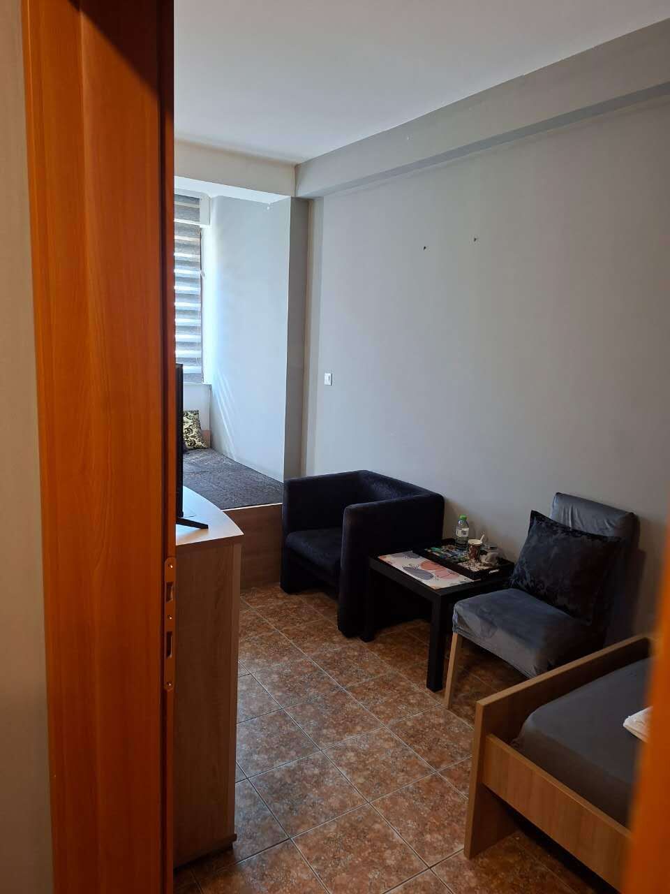 A small, furnished room with a bed, a chair, a small table, and a window.