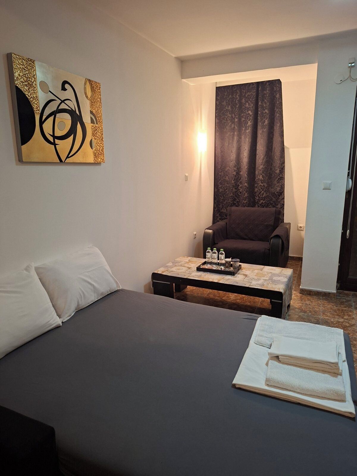 A room with a bed, a table with a tray of items, a chair, and a wall-mounted artwork.