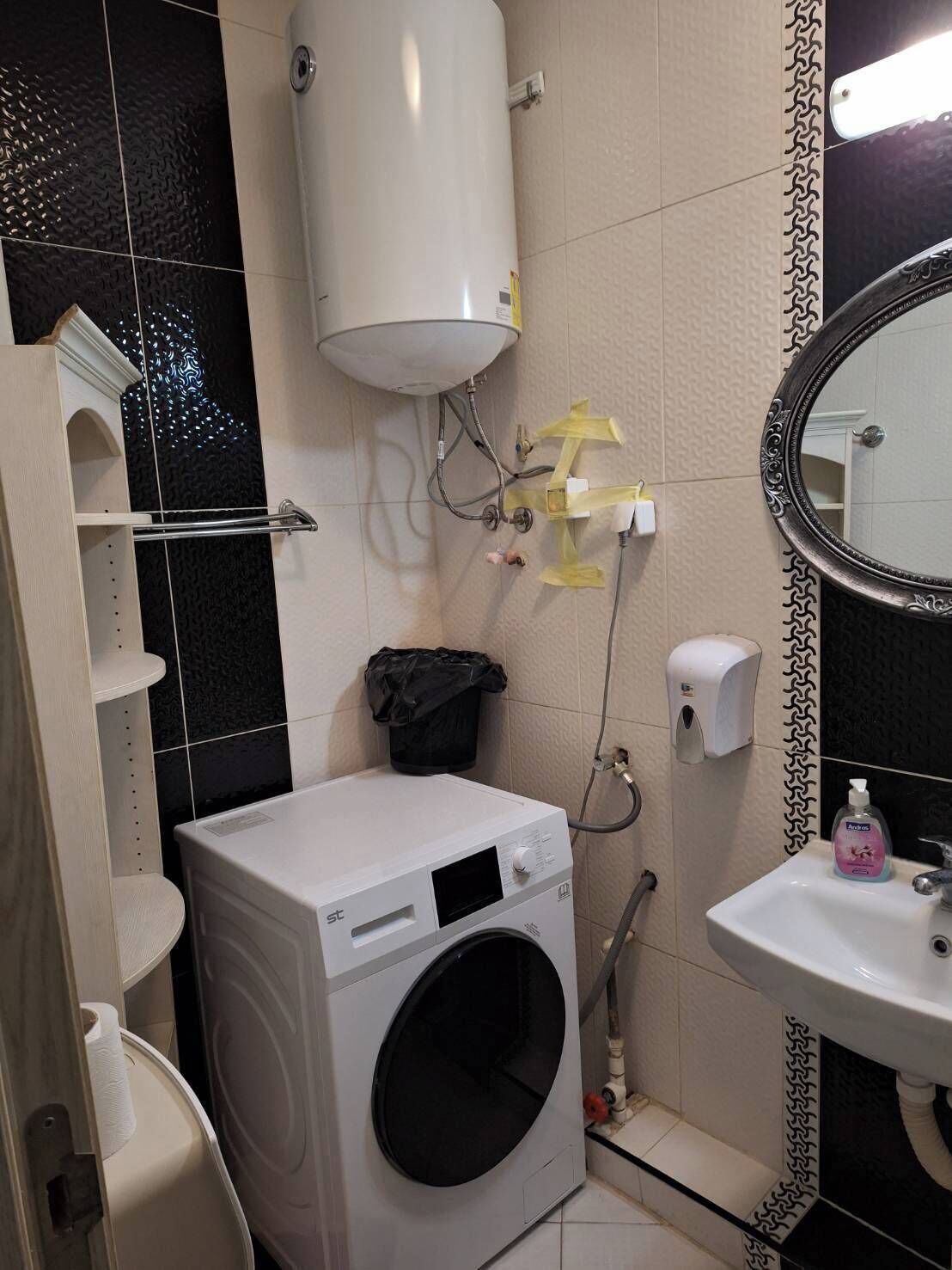 Un baño pequeño con lavadora, inodoro, lavabo y espejo.