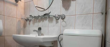 A bathroom with a white sink, toilet, and a mirror with a light fixture.